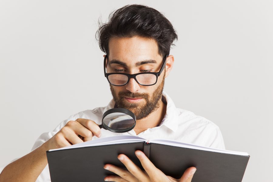 Professional young man reading with loupe and glasses