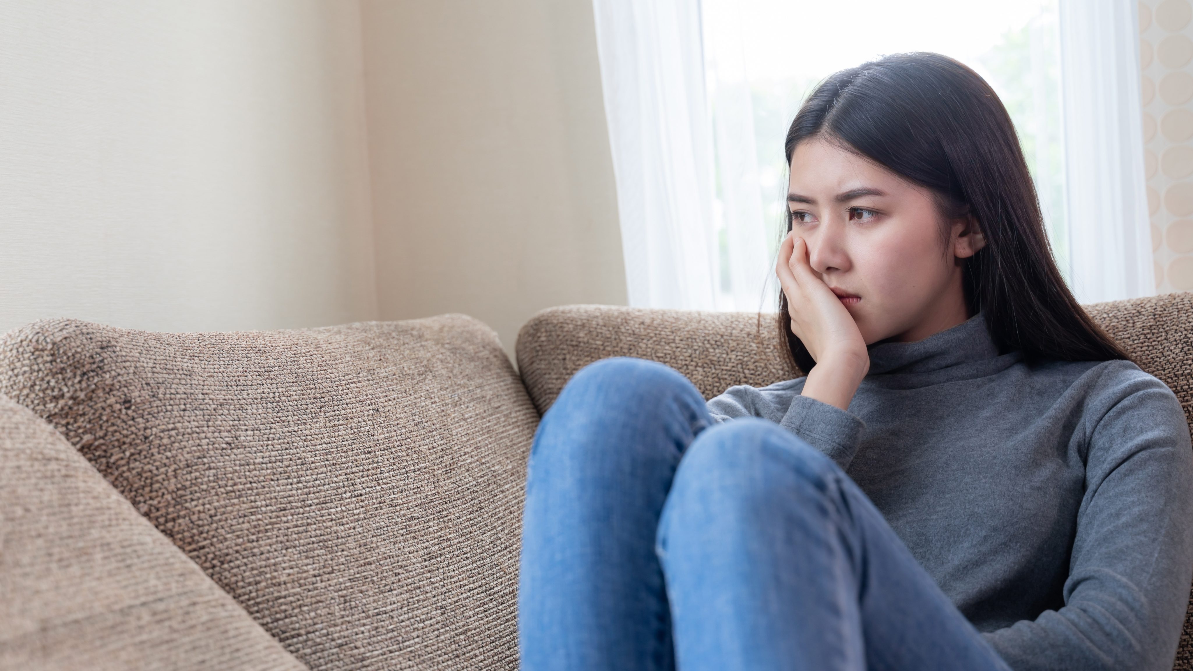 Close up face unhappy asian pretty young woman sitting alone couch