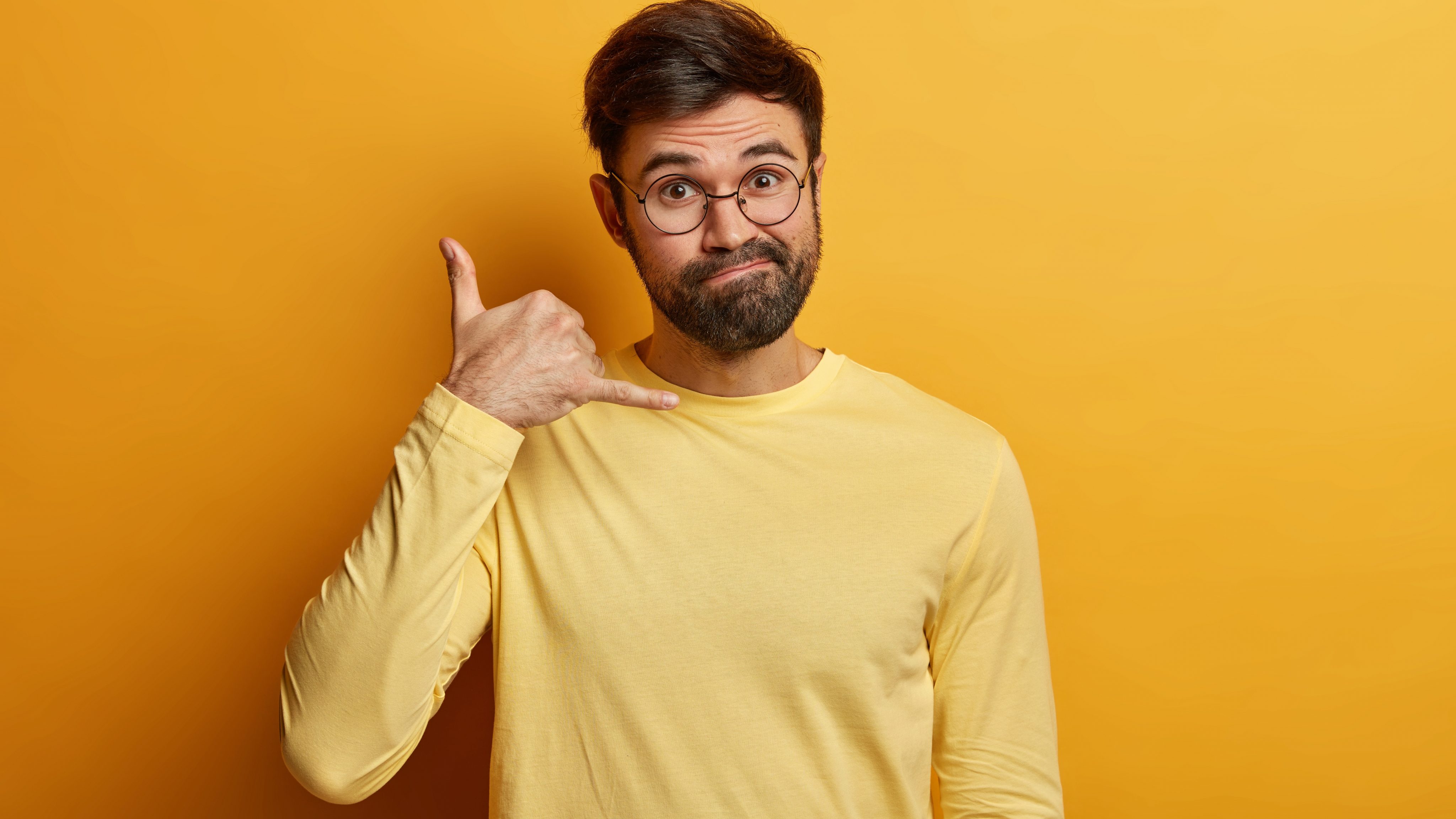 Give me call puzzled unshaven man makes call gesture with fingers asks phone number says meet time dressed casually wears casual jumper isolated yellow wall body language