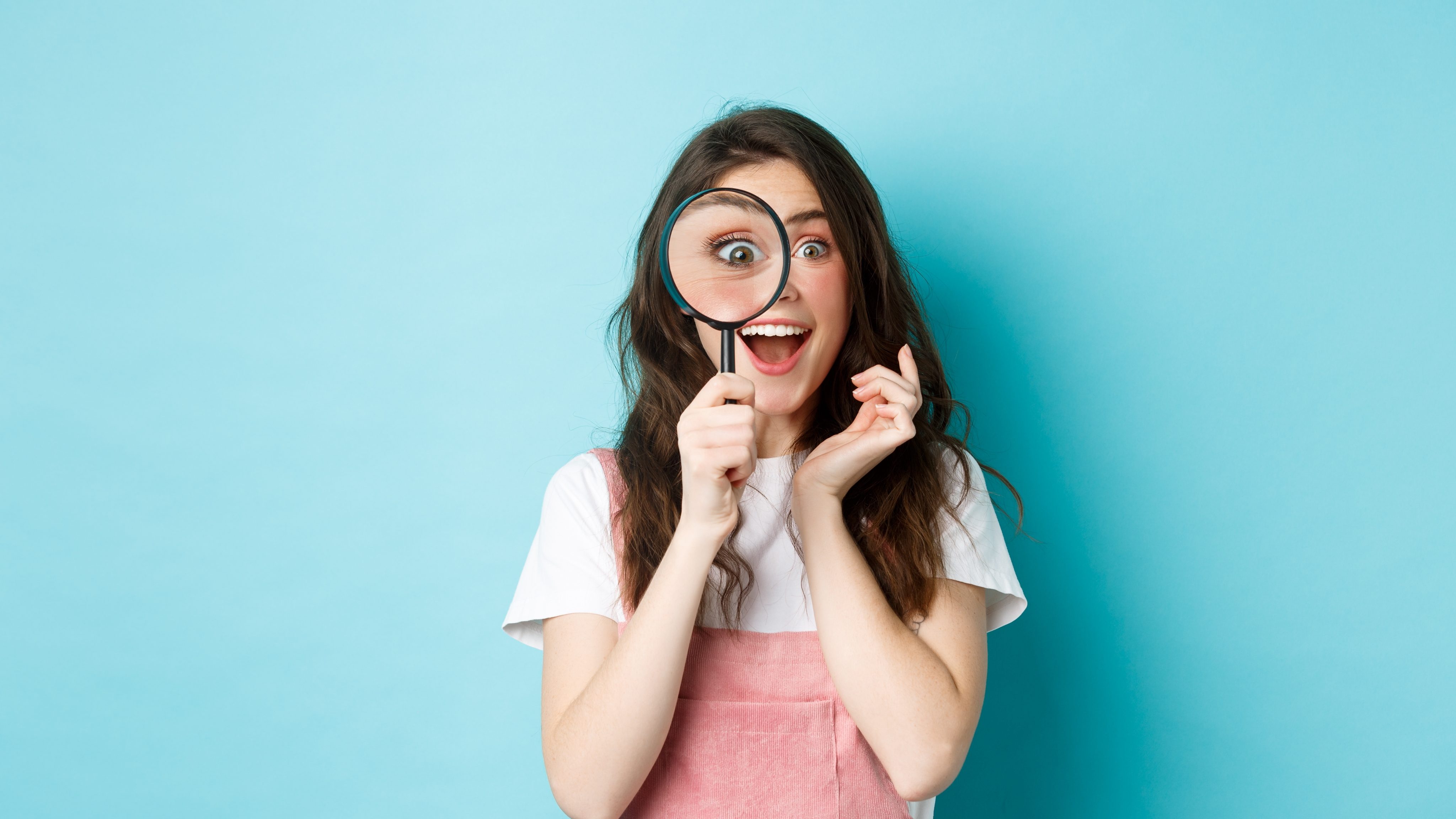Happy young woman looking through magnifying glass with excited face found search something standing blue background