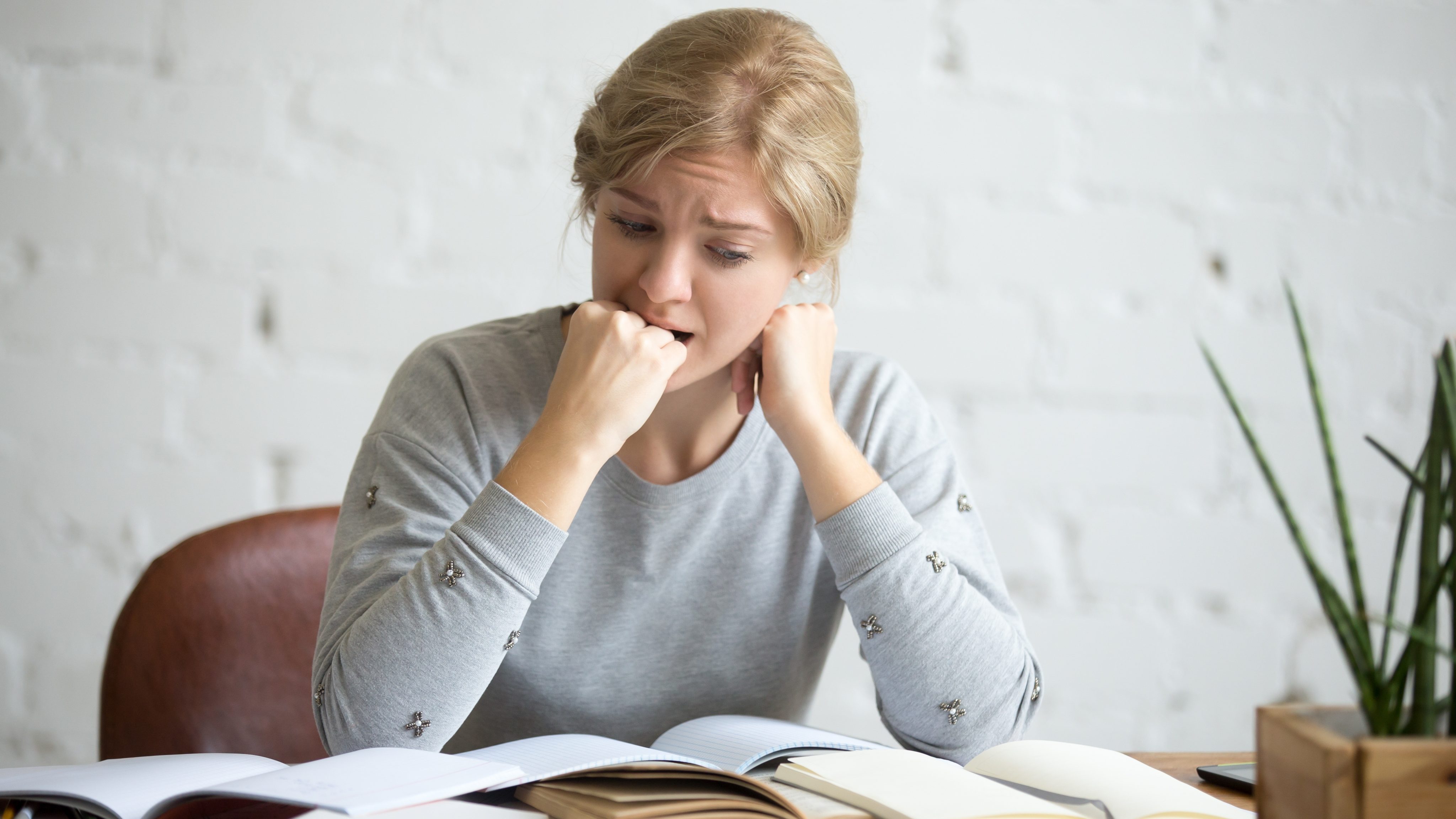 Portrait student girl sitting desk biting her fist